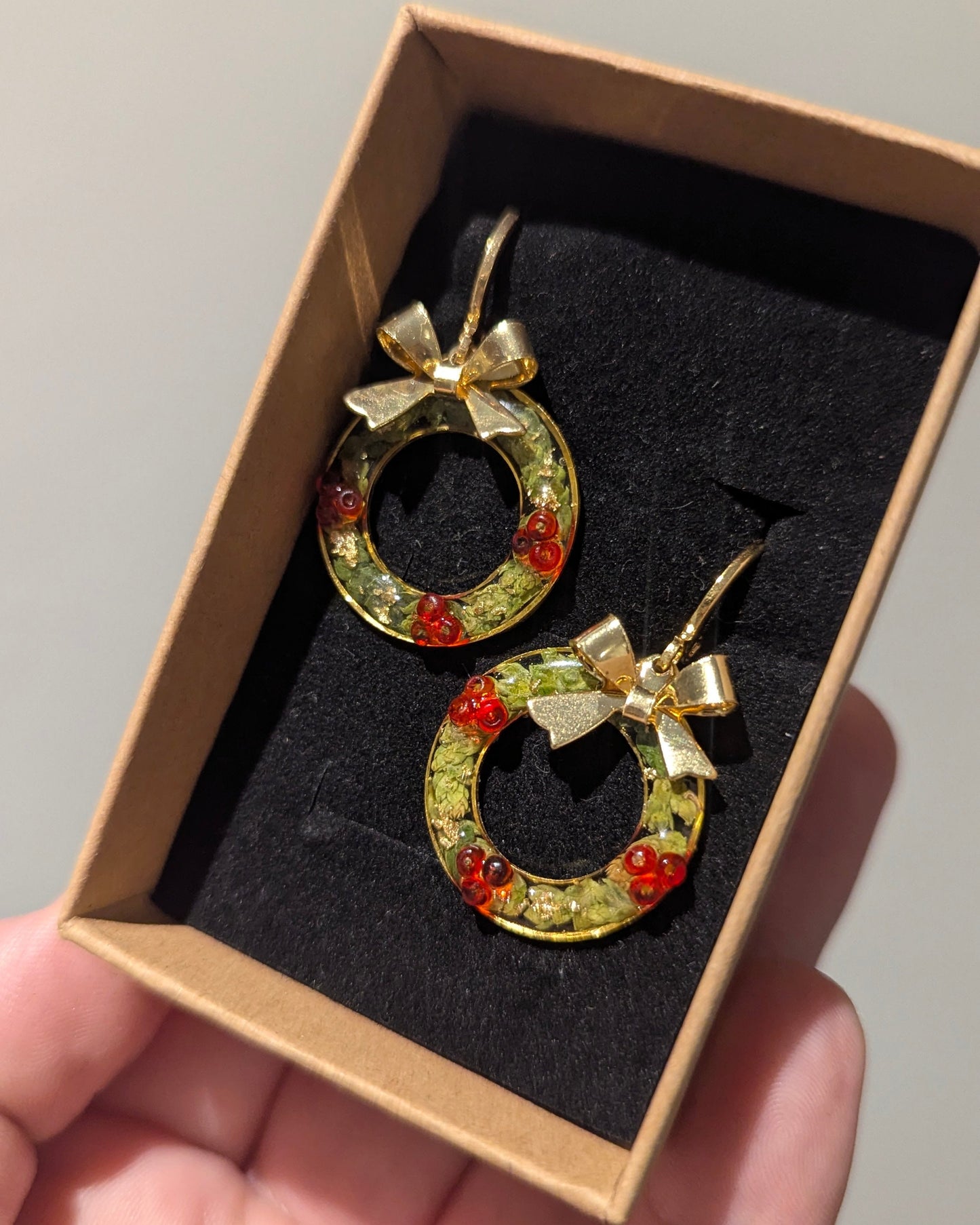 Gold hoop earrings with red stones and bows in a box held by a hand.