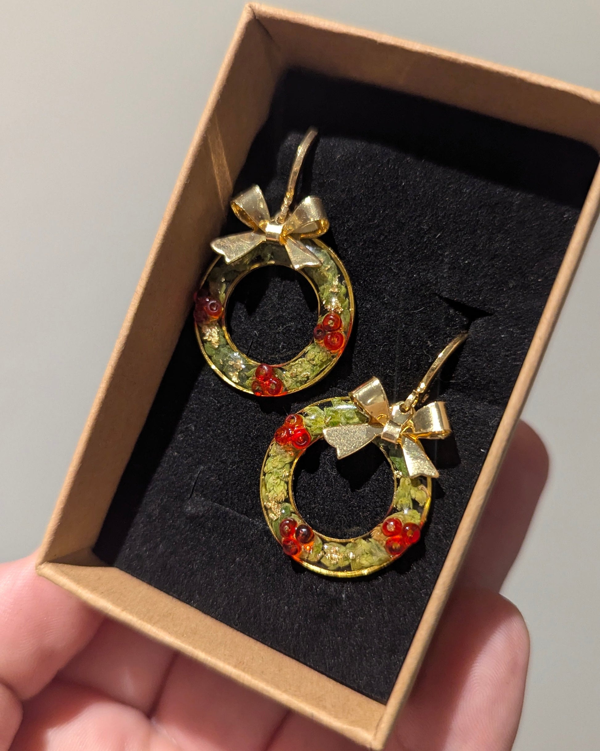 Gold hoop earrings with red stones and bows in a box held by a hand.